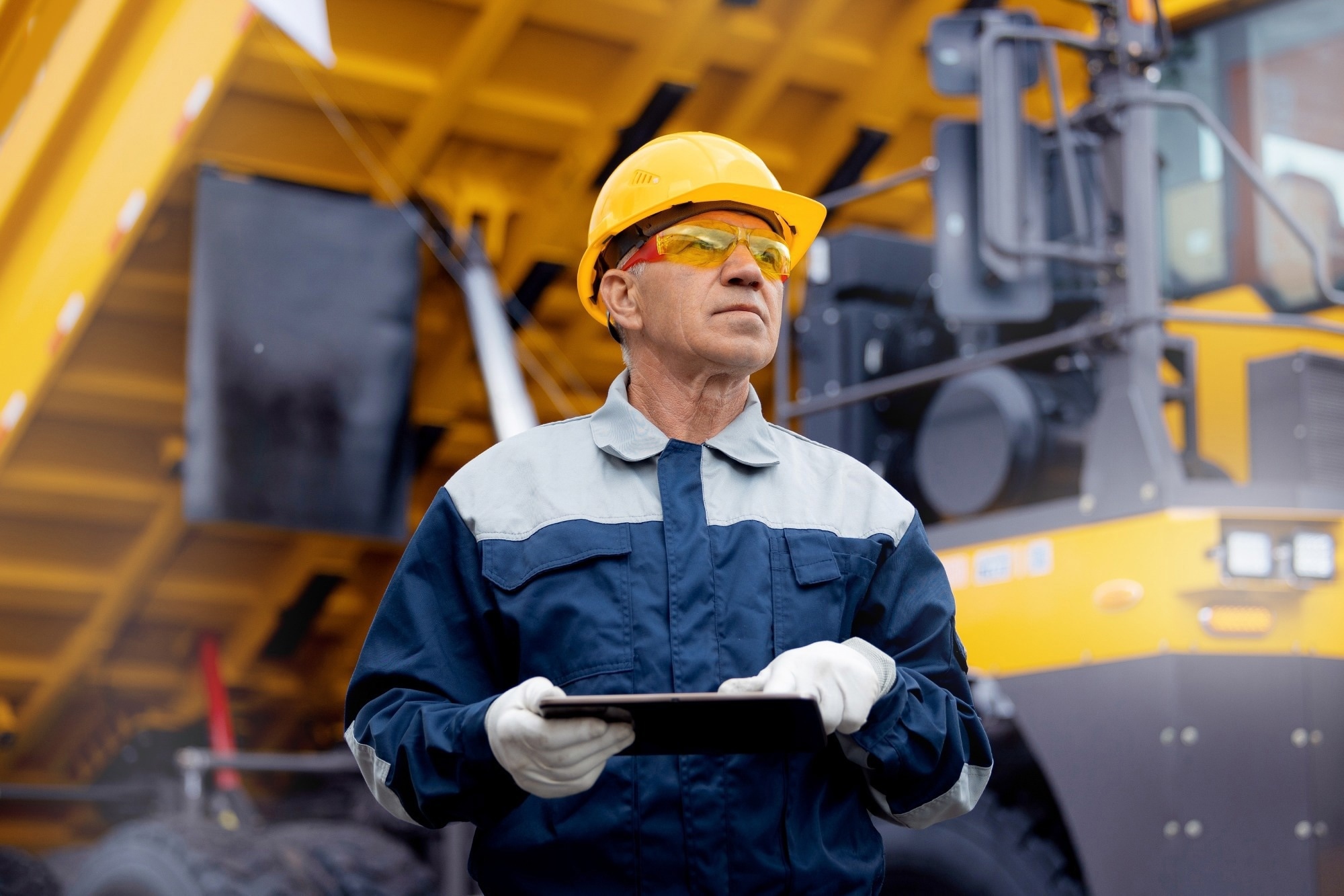 A man stands at a mining site with a digital screen, contemplating a decision.