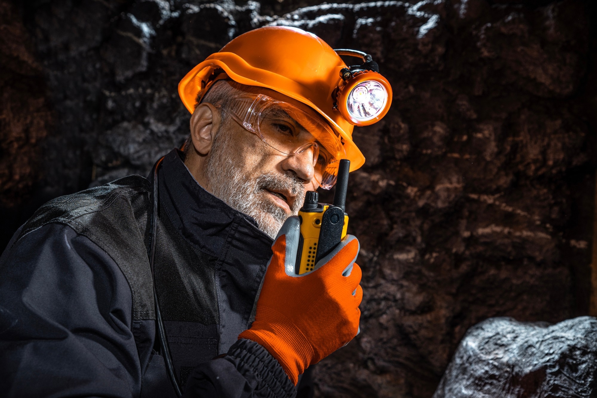 Miner in an orange hard hat using a walkie-talkie