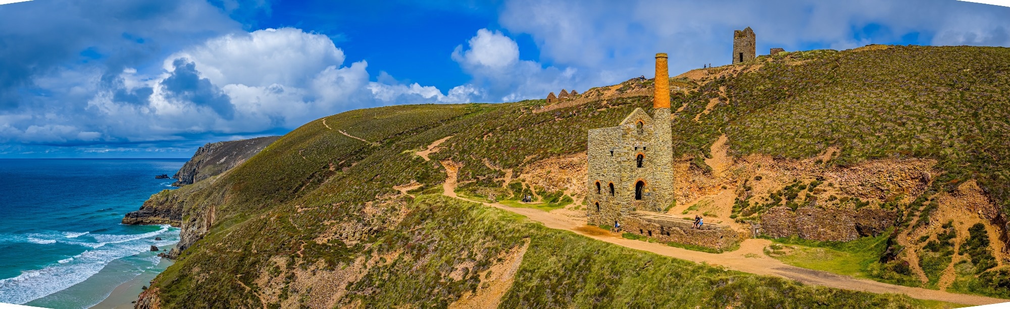 Iconic Cornish tin mine ruins on the rugged coastline with sandy beach and turquoise sea.