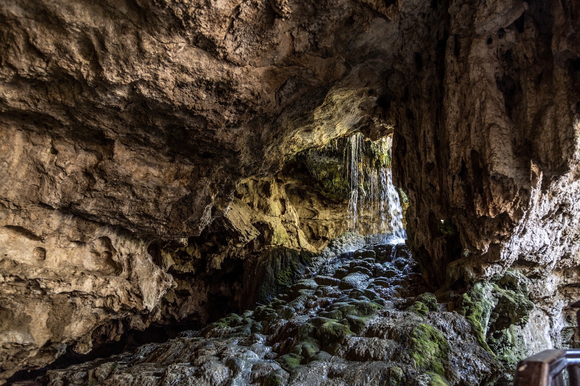 Underground waterfall cascade inside limestone cave tunnel with green moss rock. Kaklik cavern interior with water stream, geological landmark under day light, Denizli, Anatolia, Turkey.